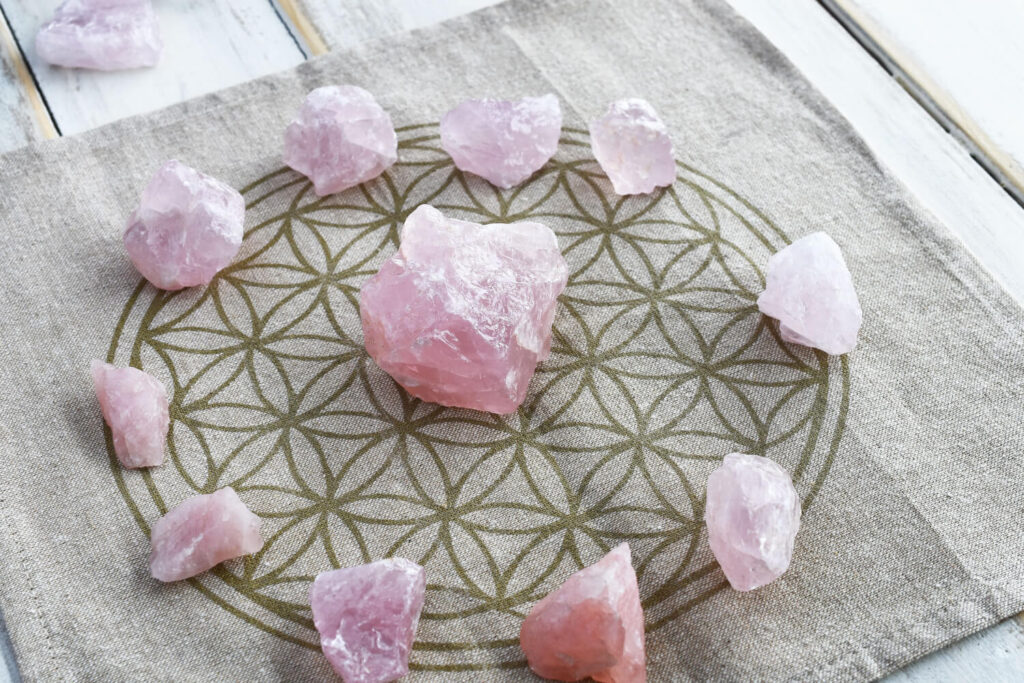 Pink rose quartz crystals arranged on a light beige linen cloth with a flower of life pattern.