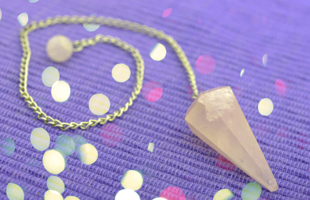 Rose quartz pendulum on purple fabric.