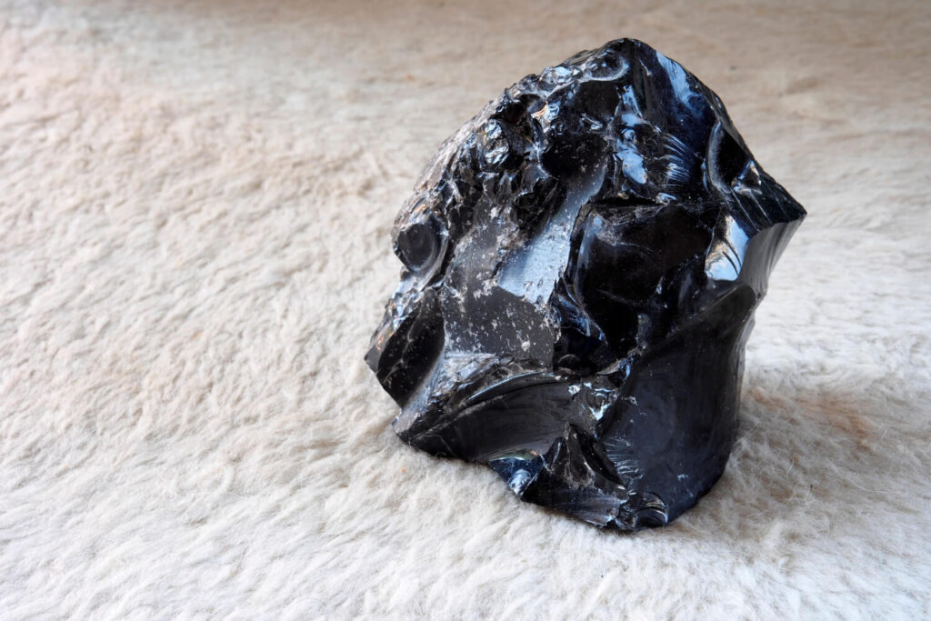 Black volcanic rock, obsidian, on a light beige surface.